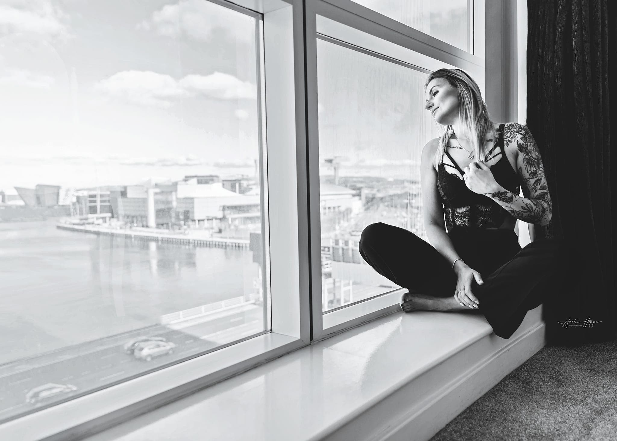 Karolina Gosz seated beside a window in a cinematic monochrome frame with softened daylight and quiet movement